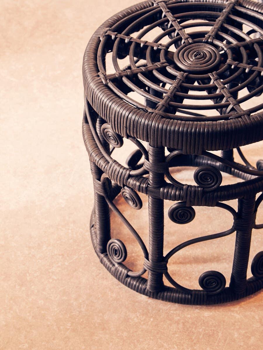 Brown rattan side table with circular woven top and decorative scrollwork on tiled floor