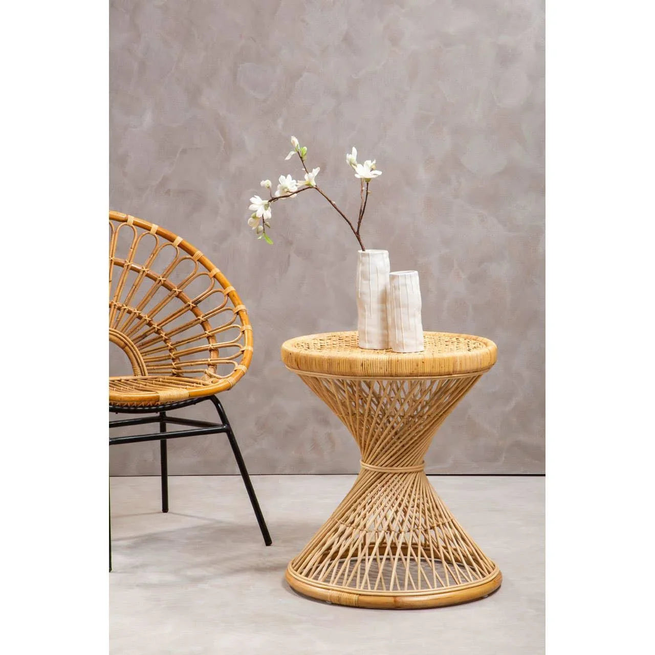Round rattan side table with decorative vases beside matching rattan chair