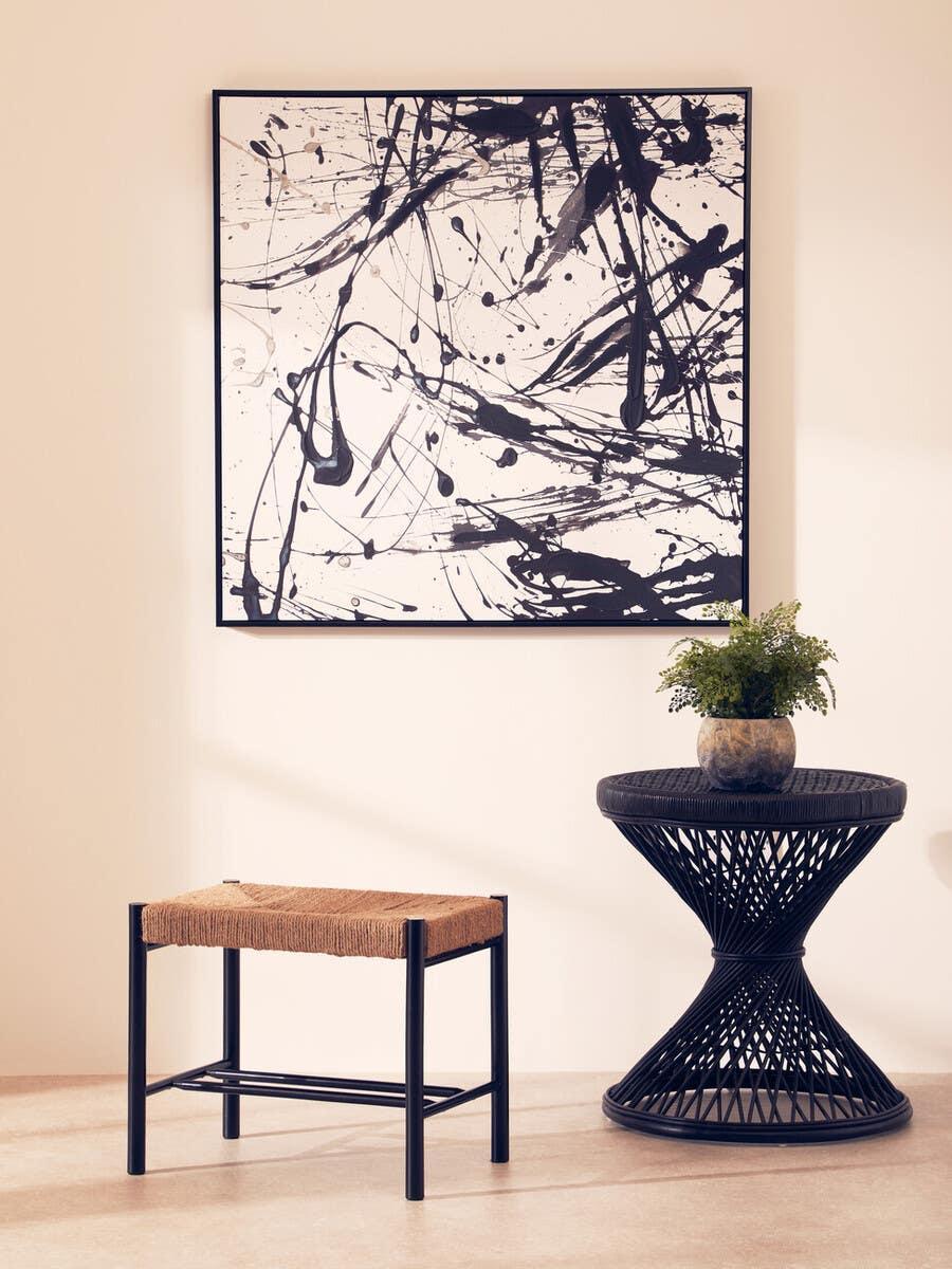 Black woven side table with plant, natural woven stool and monochrome abstract wall art