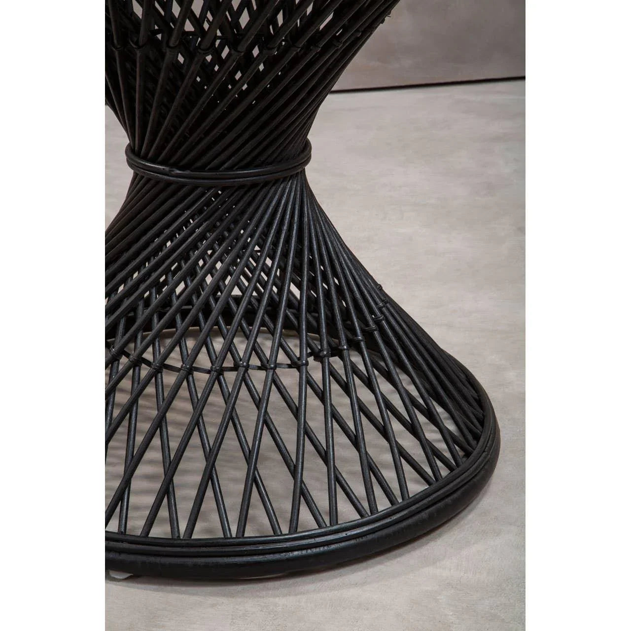 Black rattan table base with geometric open weave detail on light floor
