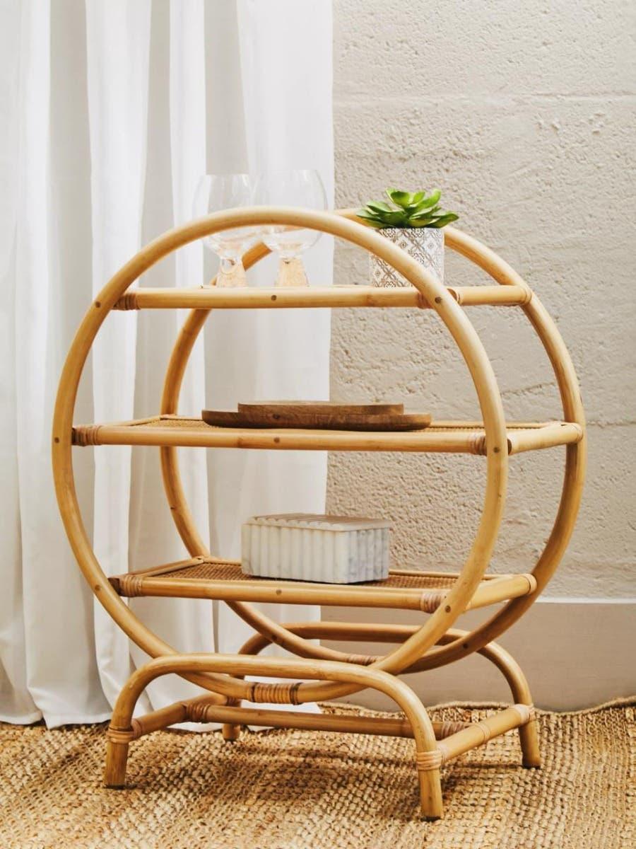 Round rattan side table with three shelves holding glassware, plant, and decor accents