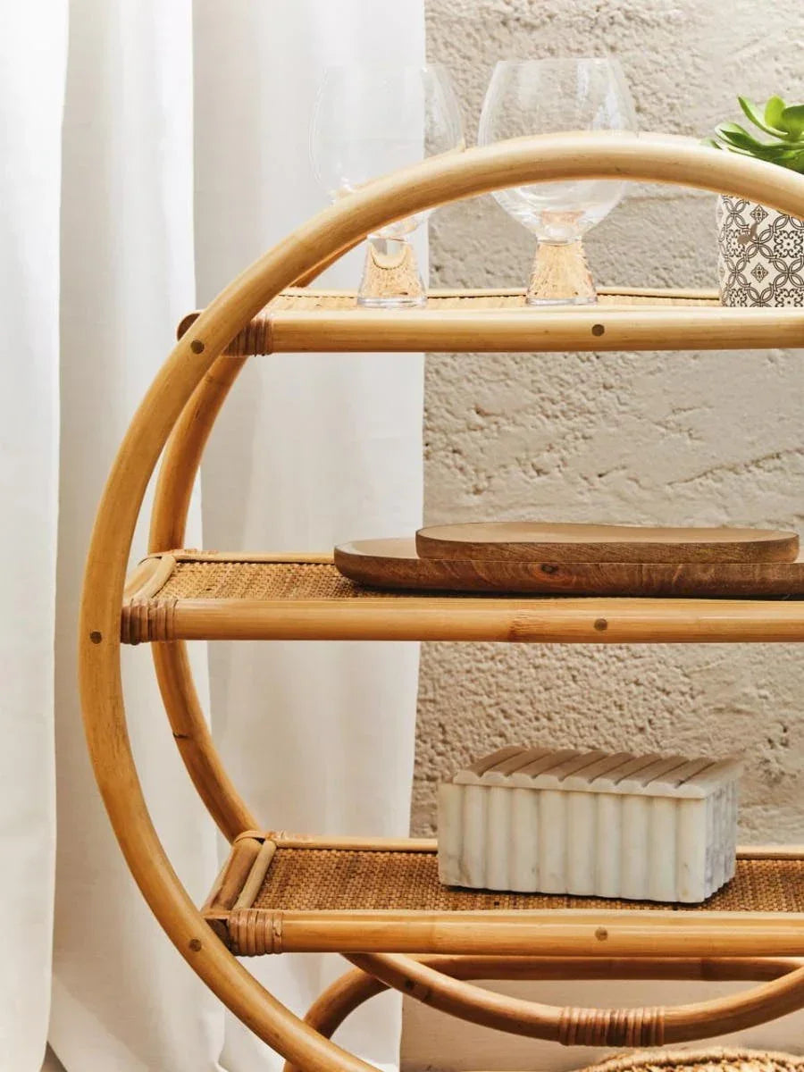 Round rattan shelving unit with glassware, decorative plant, and marble box on shelves