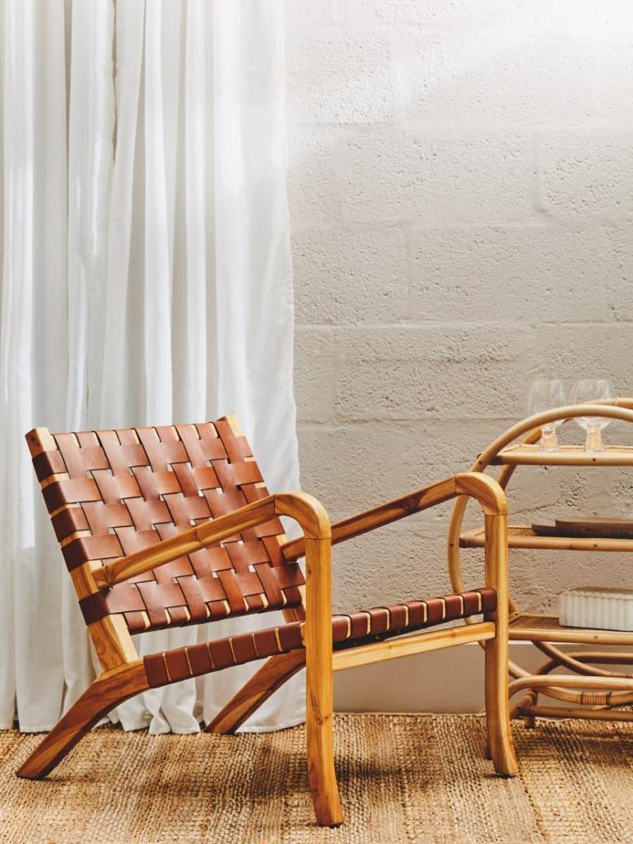 Wooden accent chair with woven brown leather seat and backrest next to side table on rug