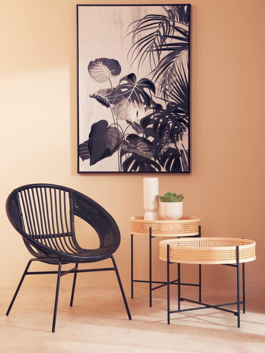 Black rattan chair with round wicker side tables and botanical wall art in modern living space