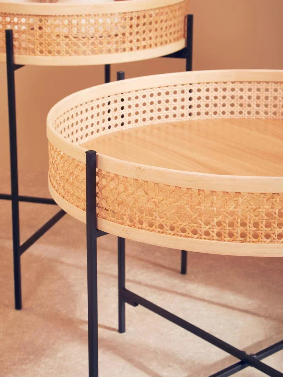 Round rattan side tables with cane webbing and black metal legs on beige floor
