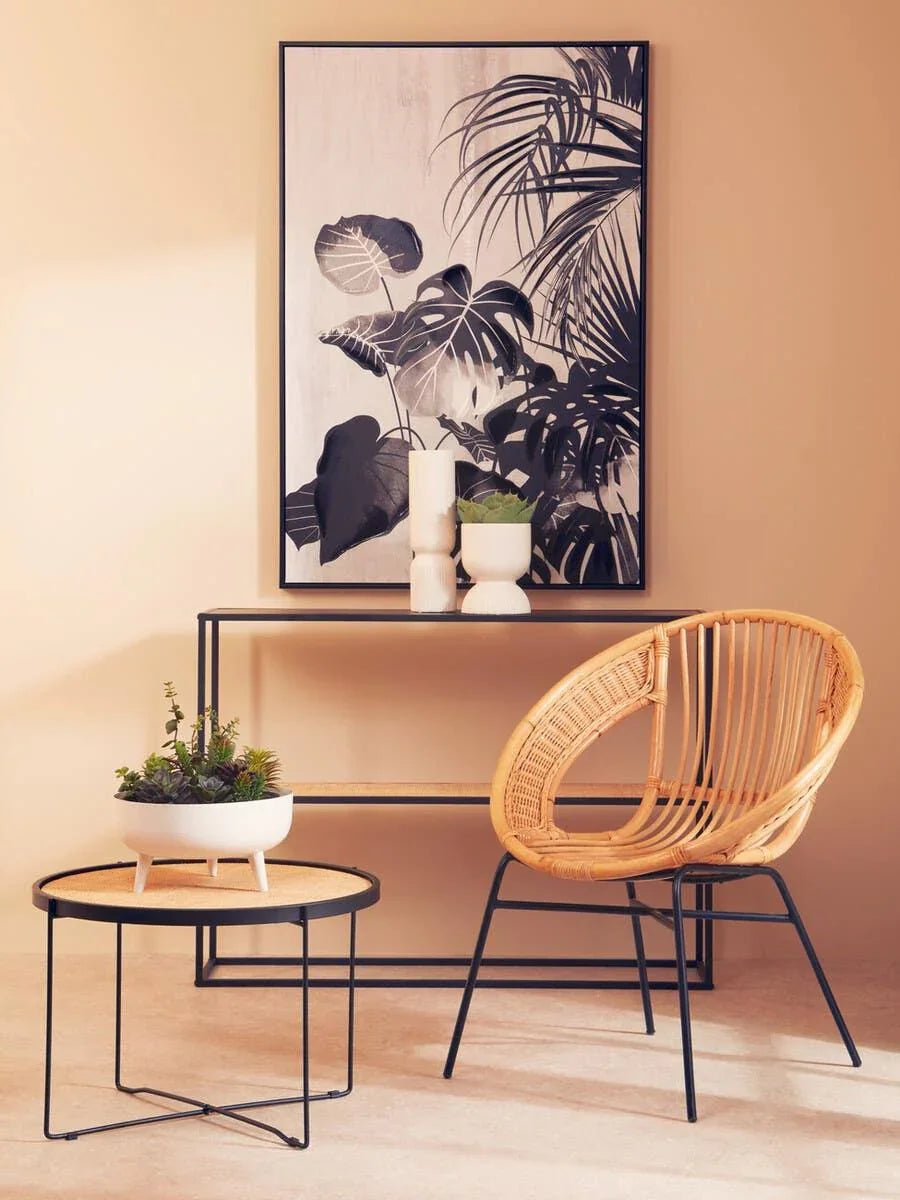 Rattan accent chair beside black metal console table and round side table with planter