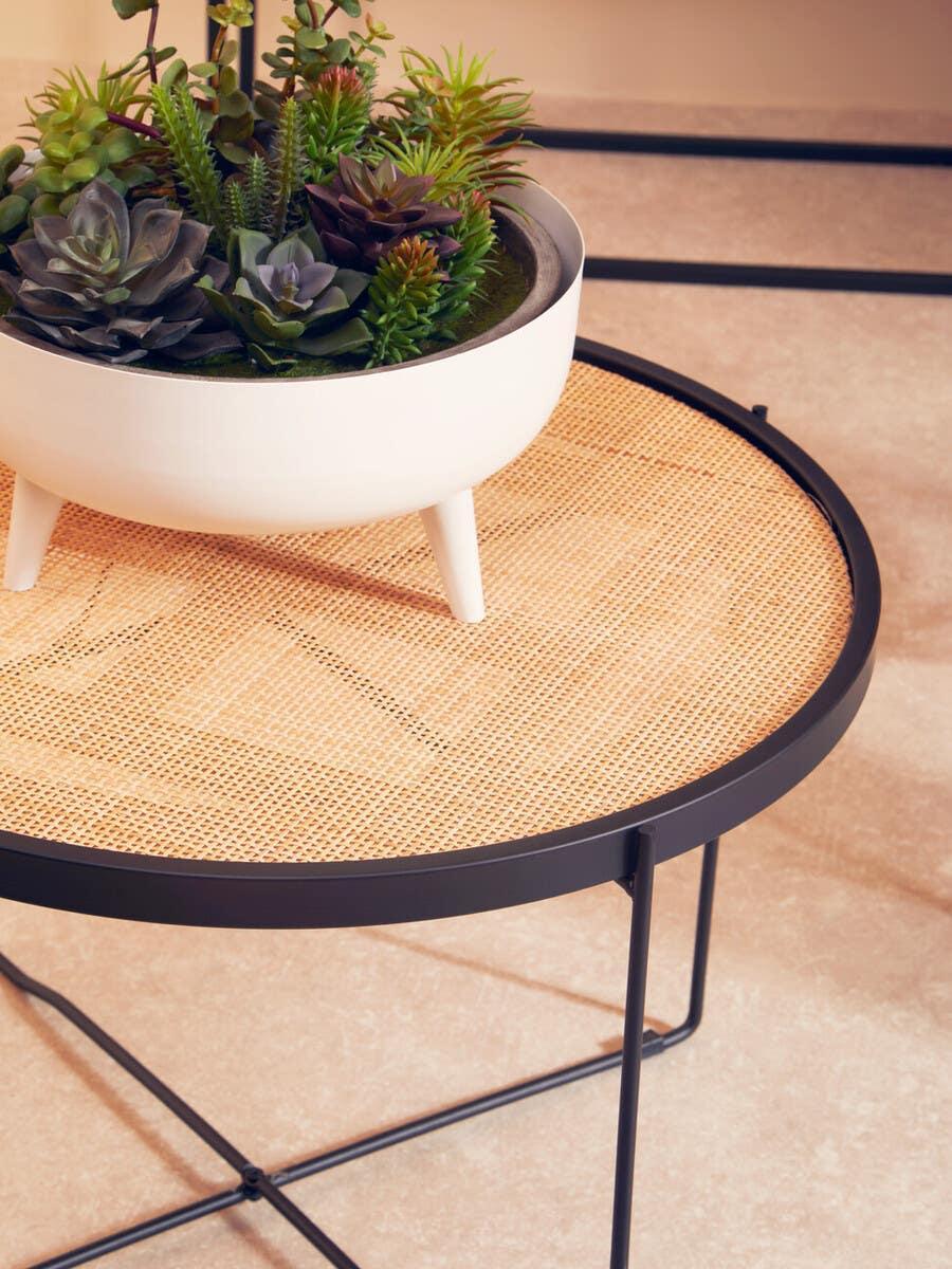 Round rattan side table with black metal frame and white planter with artificial succulents