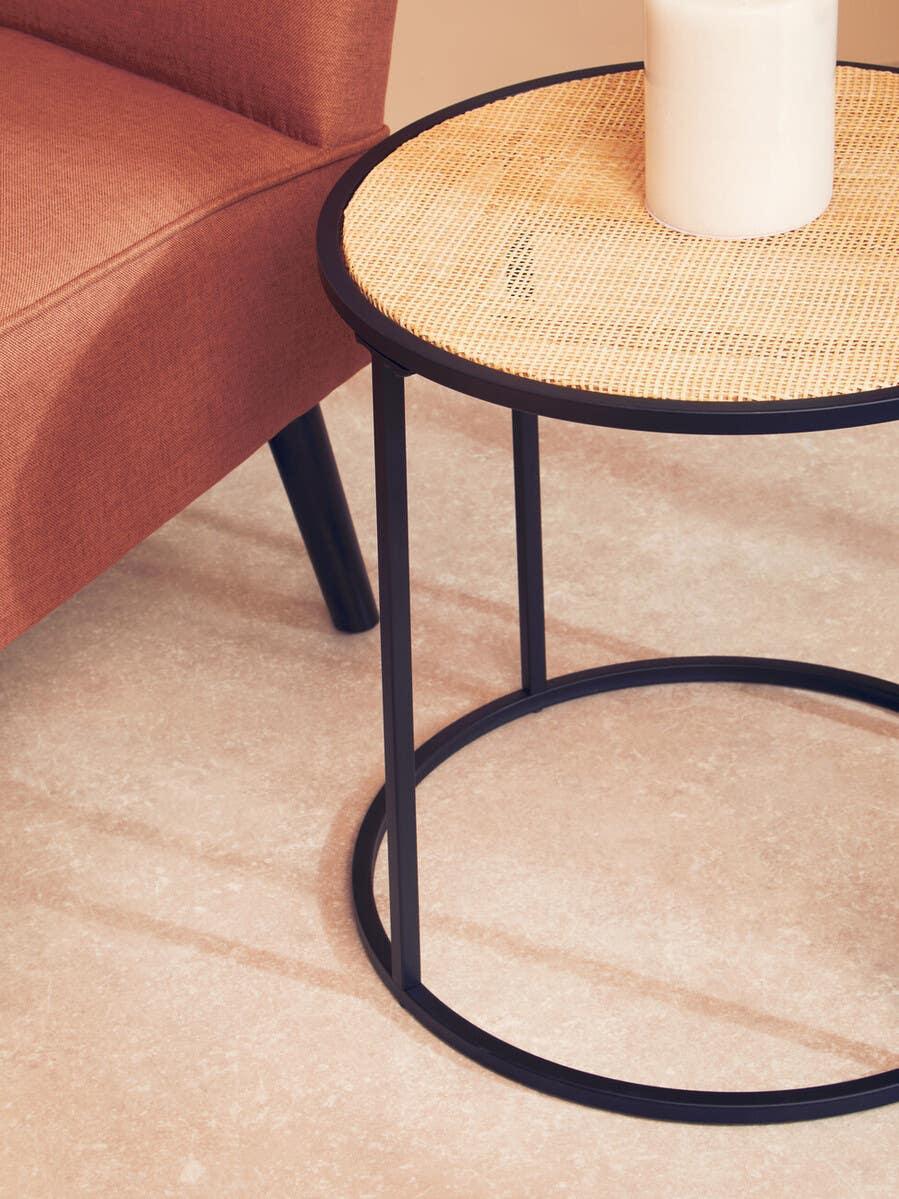 Round rattan side table with black metal frame beside terracotta fabric armchair