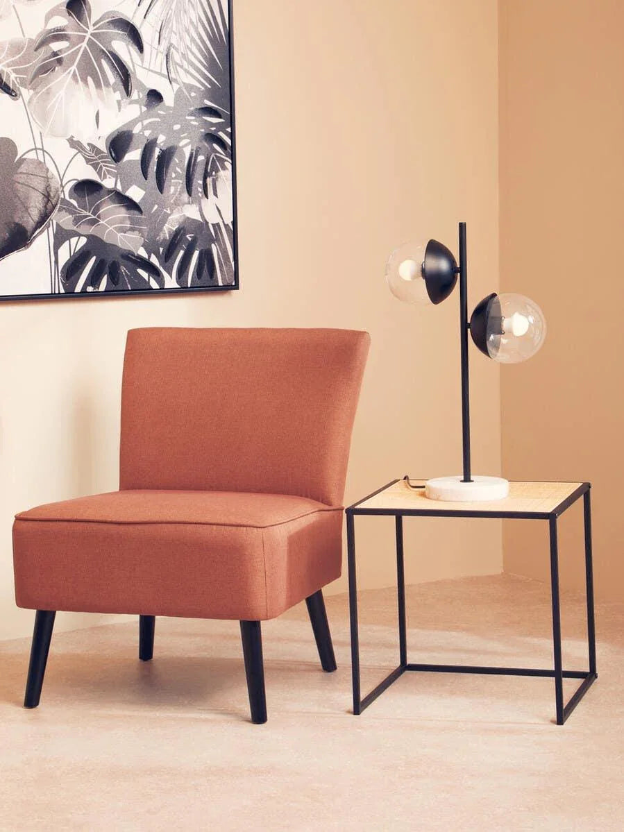 Rust accent chair with black legs beside a modern side table and globe lamp