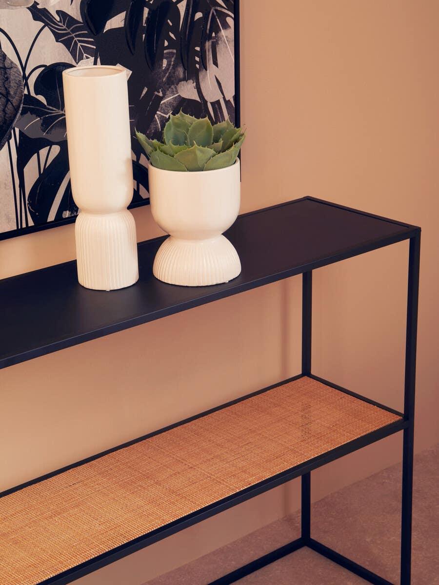 Black metal console table with rattan shelf, decorative vases, and green plant display