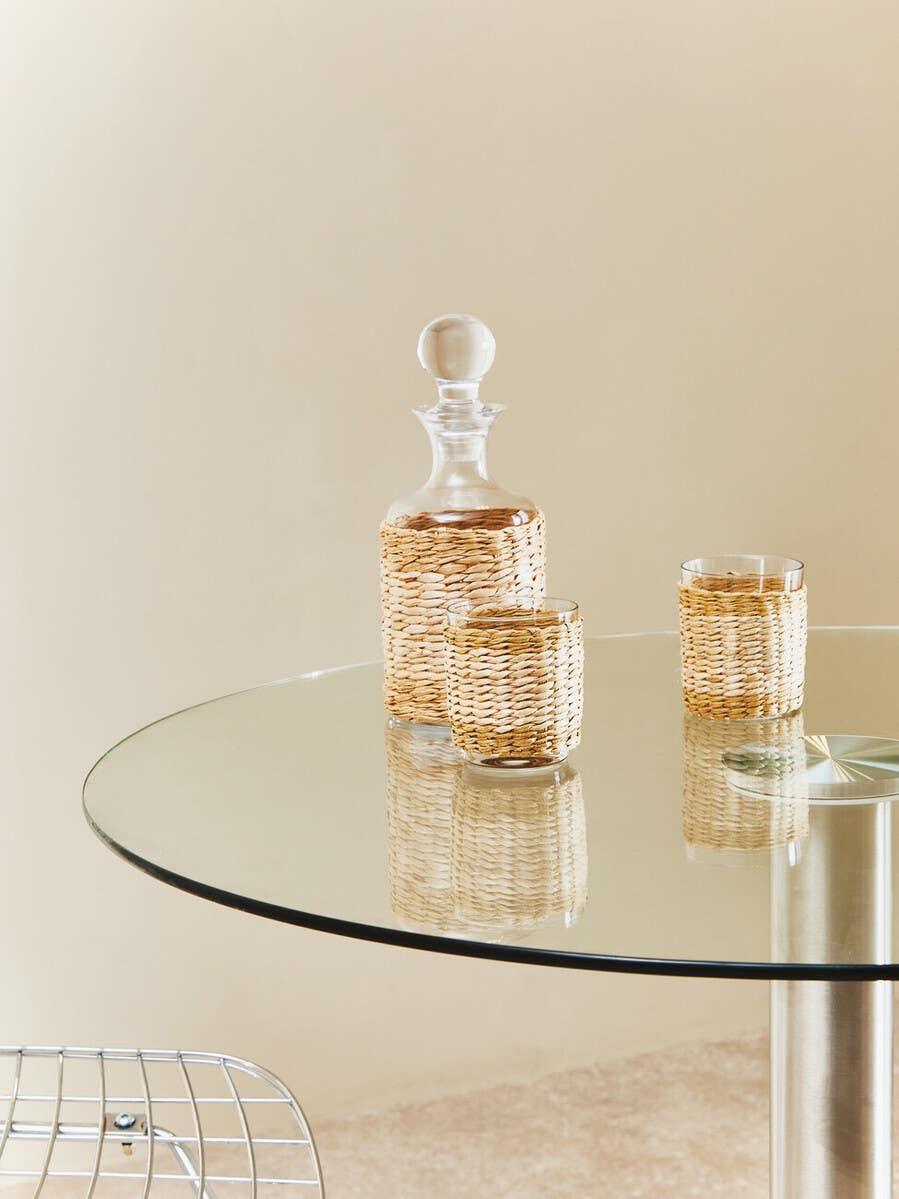 Glass decanter and two wicker-wrapped glasses on round glass dining table