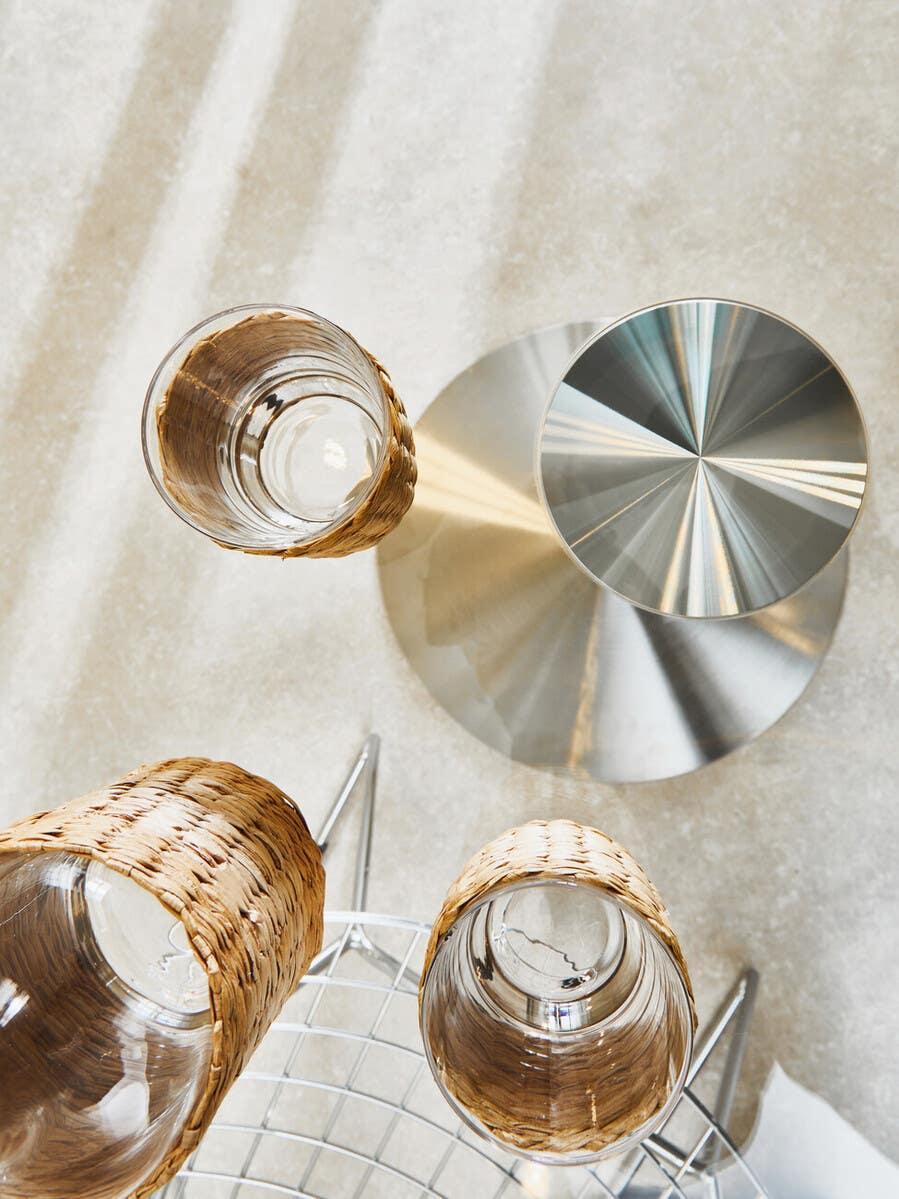 Set of three wicker wrapped drinking glasses on metal wire chair beside round metal table