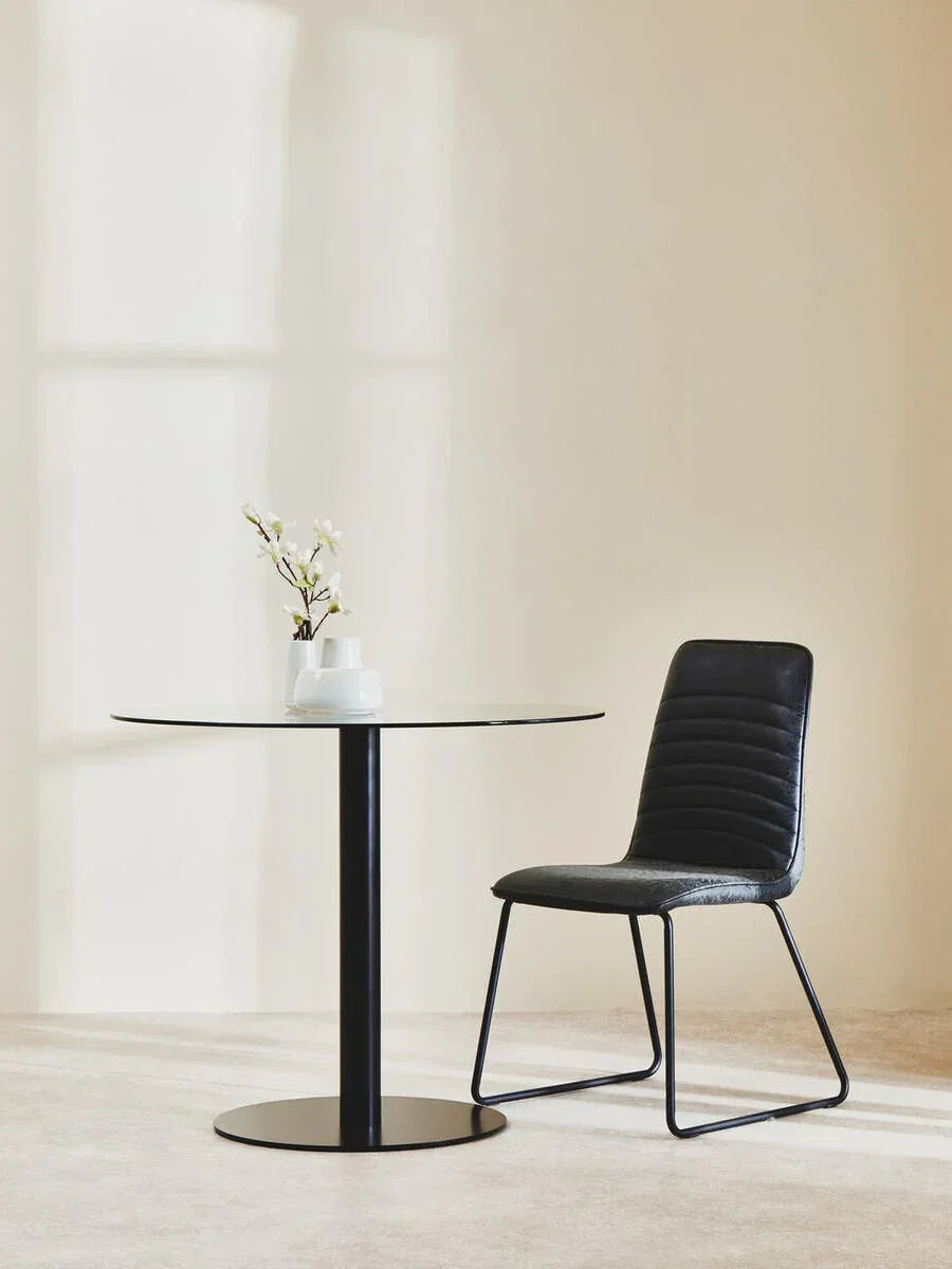 Glass dining table with black metal base and black modern chair in minimal room