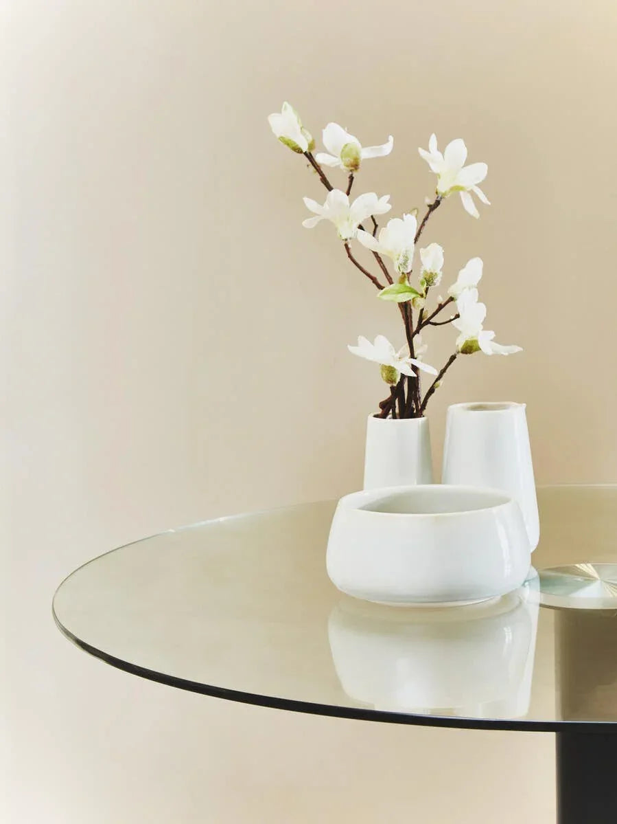 Round glass dining table with white ceramic vases and artificial flowers