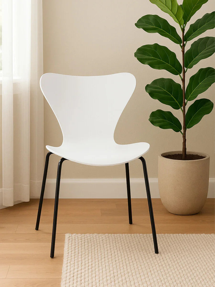 White modern dining chair with black metal legs on wooden floor beside large potted plant