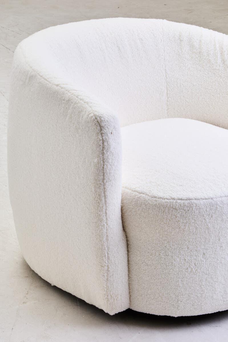 Curved boucle accent chair with plush white upholstery on concrete floor
