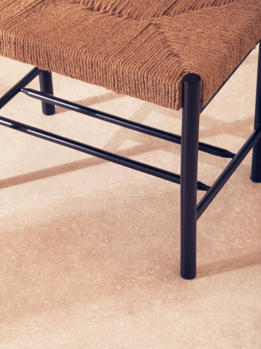 Woven seat dining chair with black metal legs on neutral floor