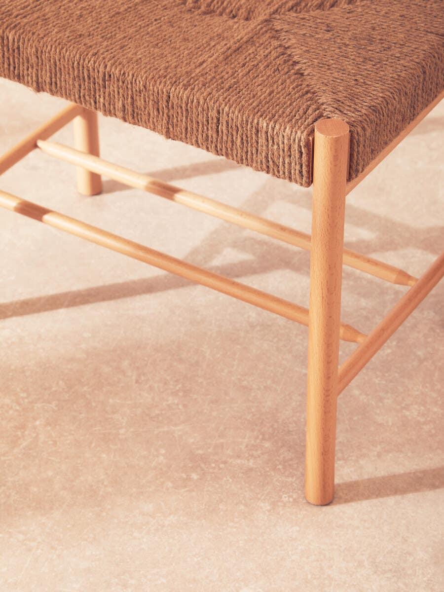 Close-up of woven rope dining chair seat with natural wood legs on tiled floor