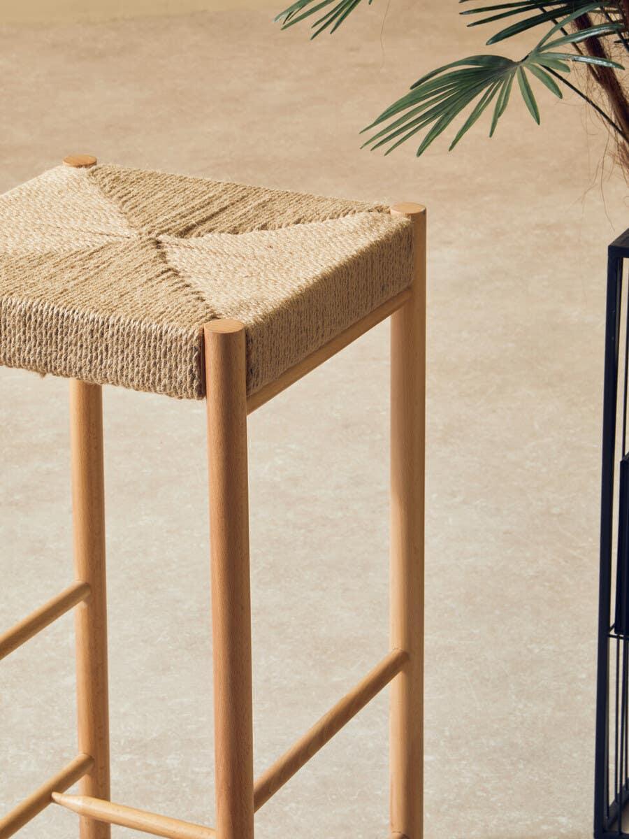 Wooden bar stool with woven natural seagrass seat detail on tile floor