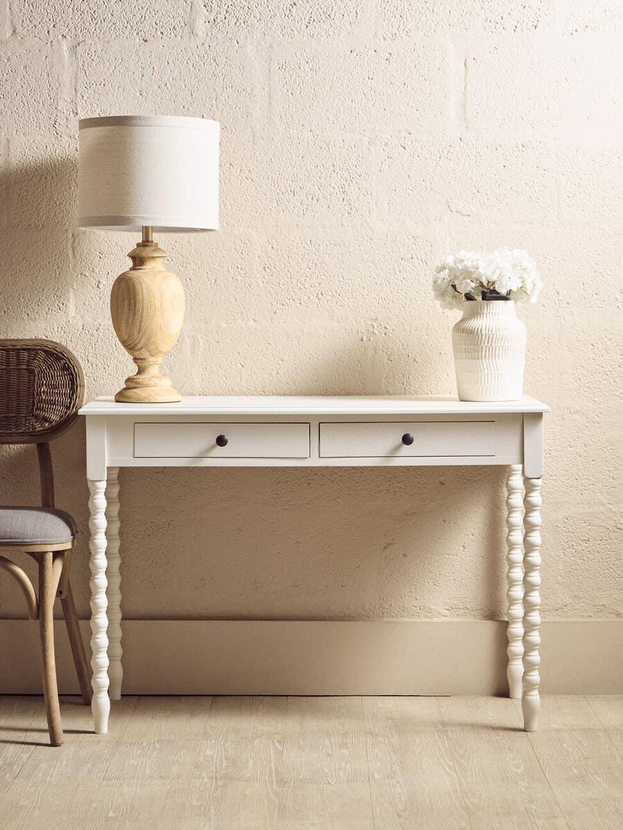 White console table with two drawers, spiral legs, lamp, and vase against beige wall