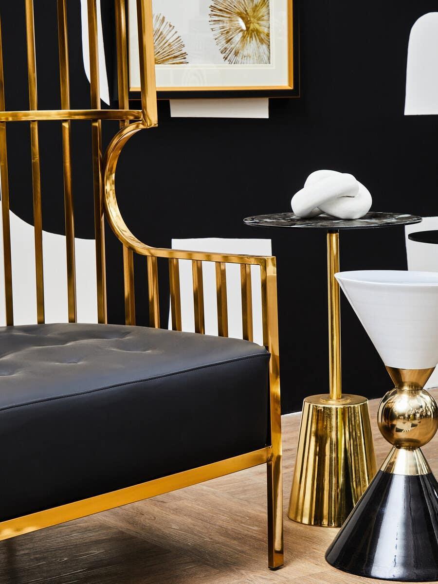 Modern gold metal accent chair with black leather seat next to marble side table and decor