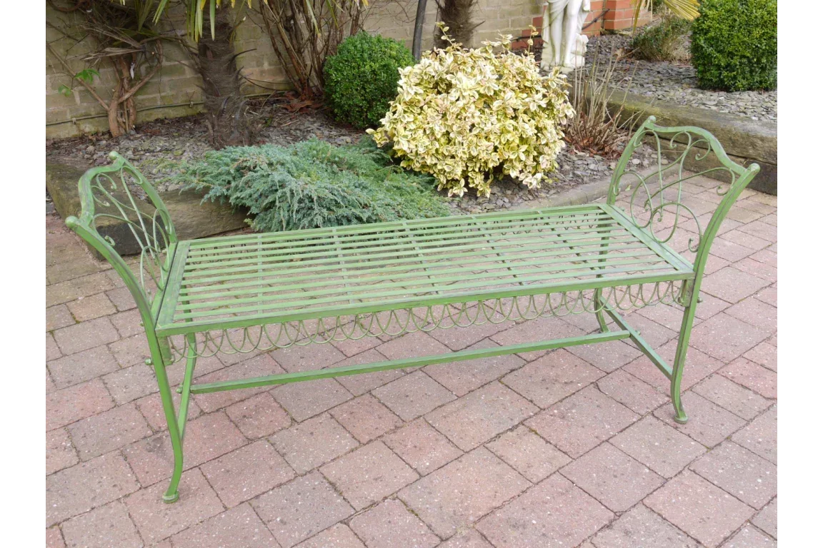 Green metal garden bench with decorative armrests on brick patio