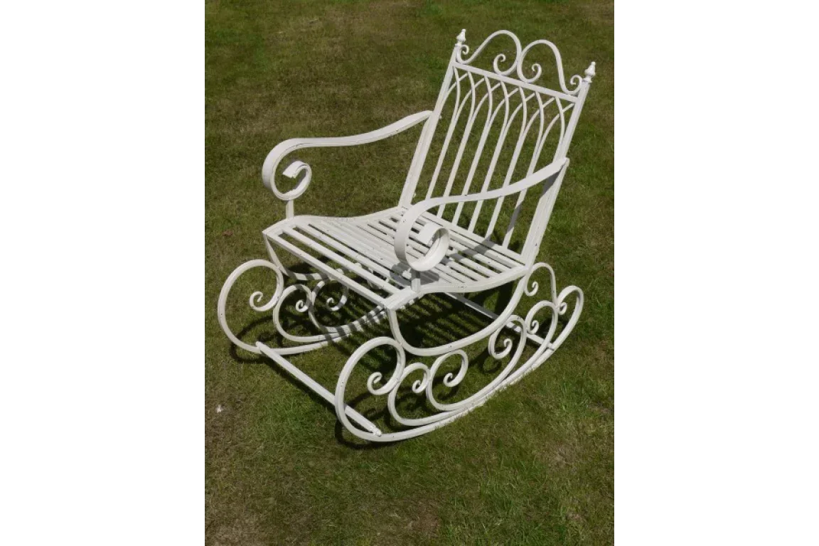 White metal garden rocking chair with decorative scrollwork on grass