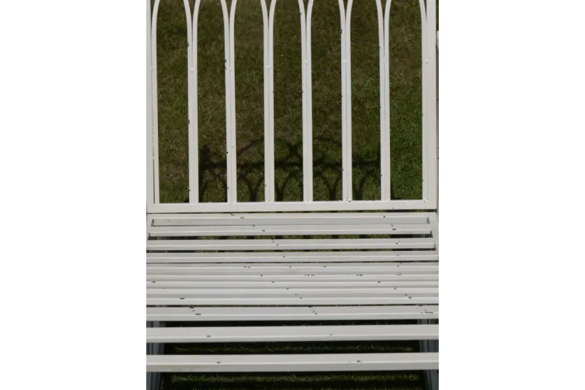 White metal garden bench with vertical slatted backrest on grass