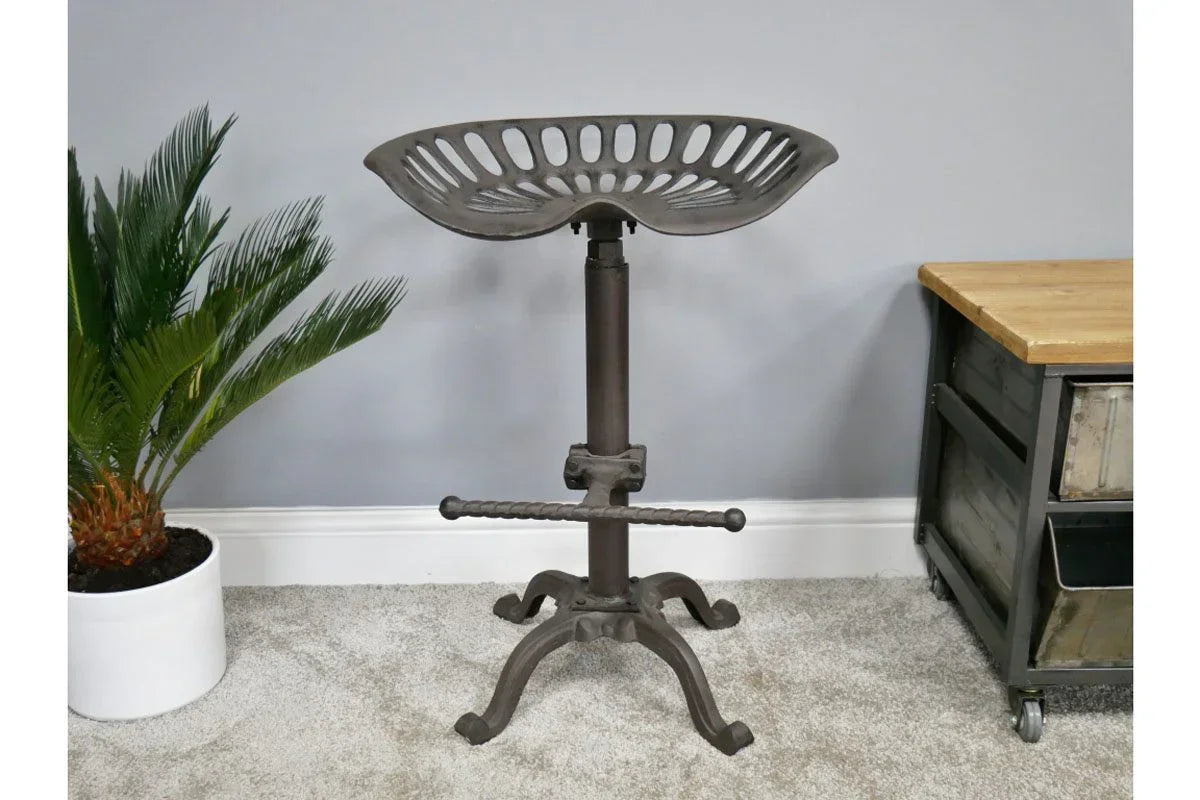 Industrial metal bar stool with tractor seat and footrest beside plant and wooden cabinet