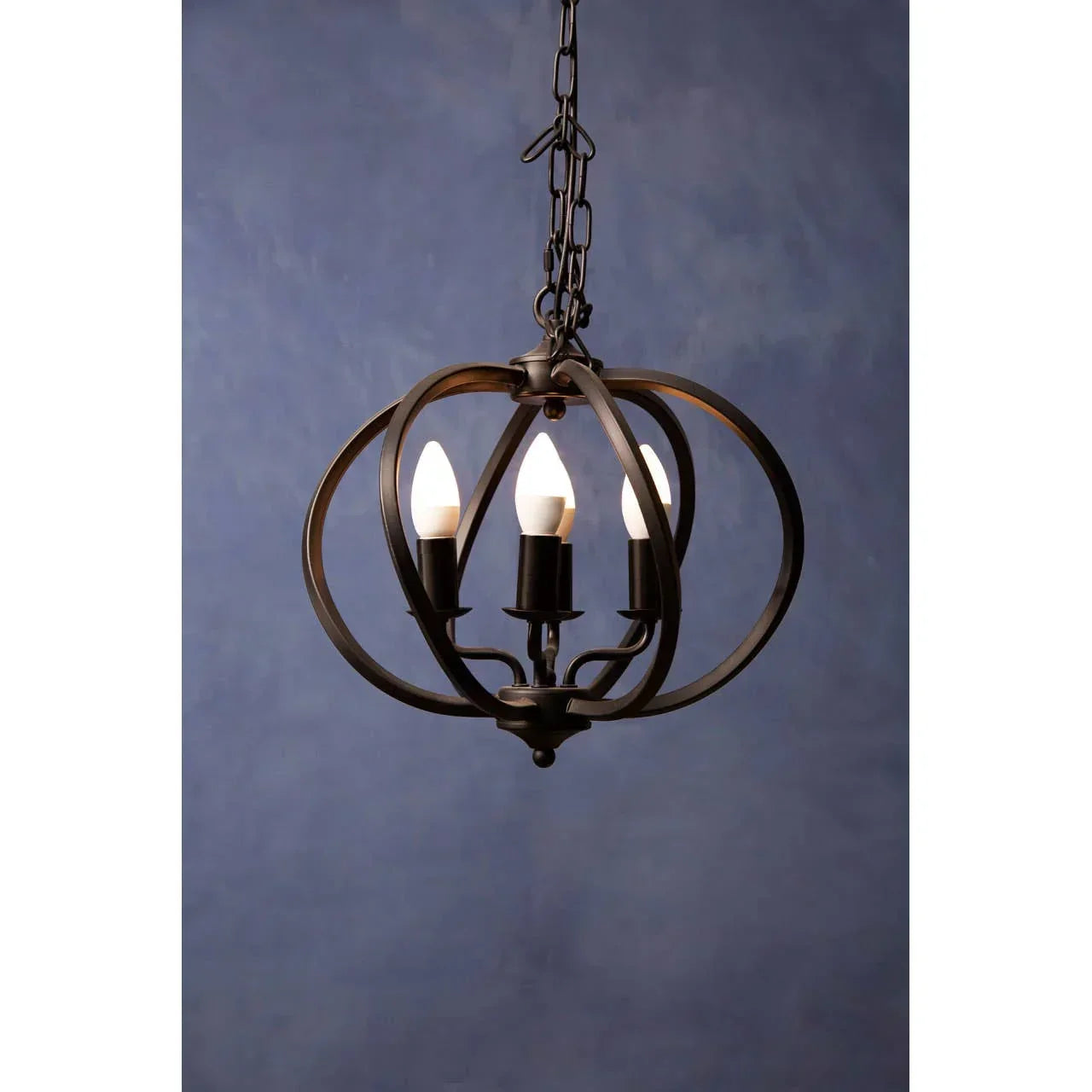 Black metal orb pendant light with three candle bulbs and chain hanging against blue wall