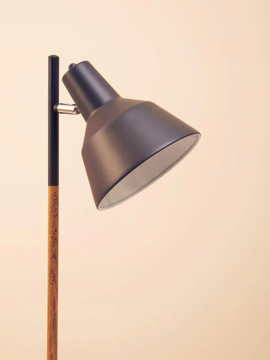 Black metal floor lamp with angled shade and wood effect stand against neutral wall