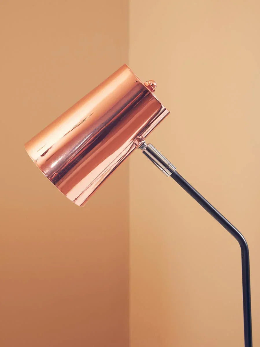 Copper floor lamp with angled black stand against beige wall