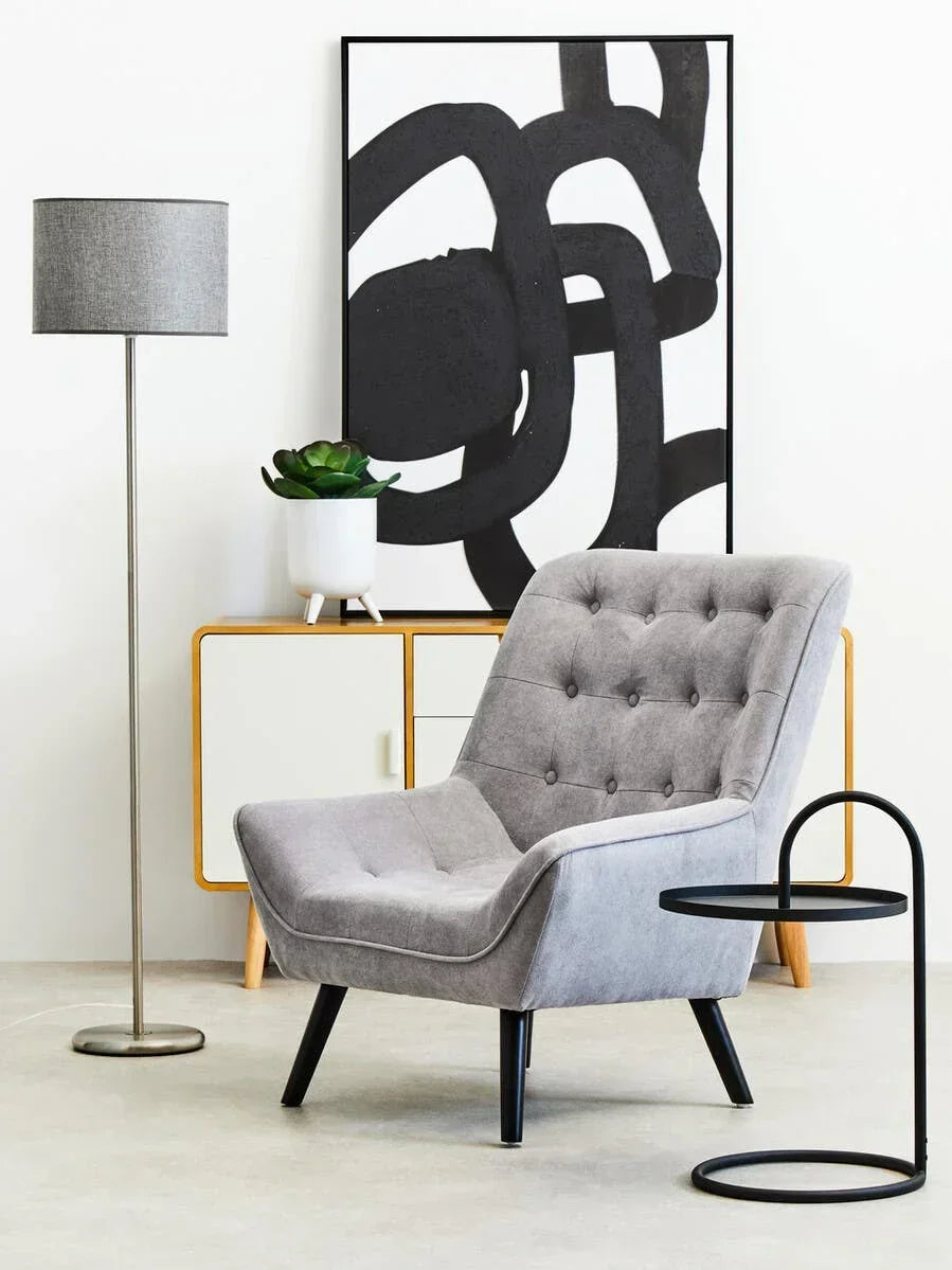 Grey accent armchair with button tufting, beside side table, lamp, and sideboard