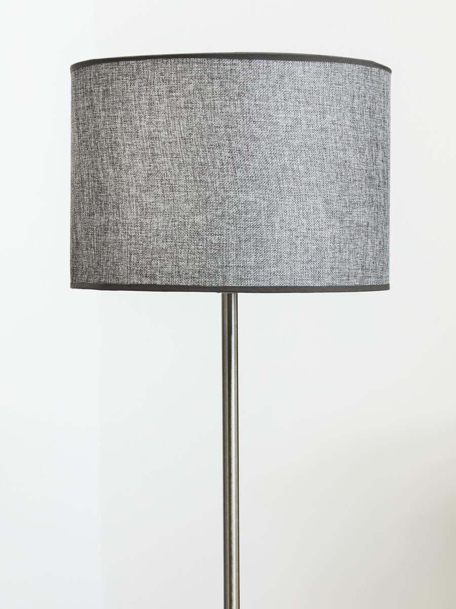 Grey fabric floor lamp with drum shade and metal stand against a white wall