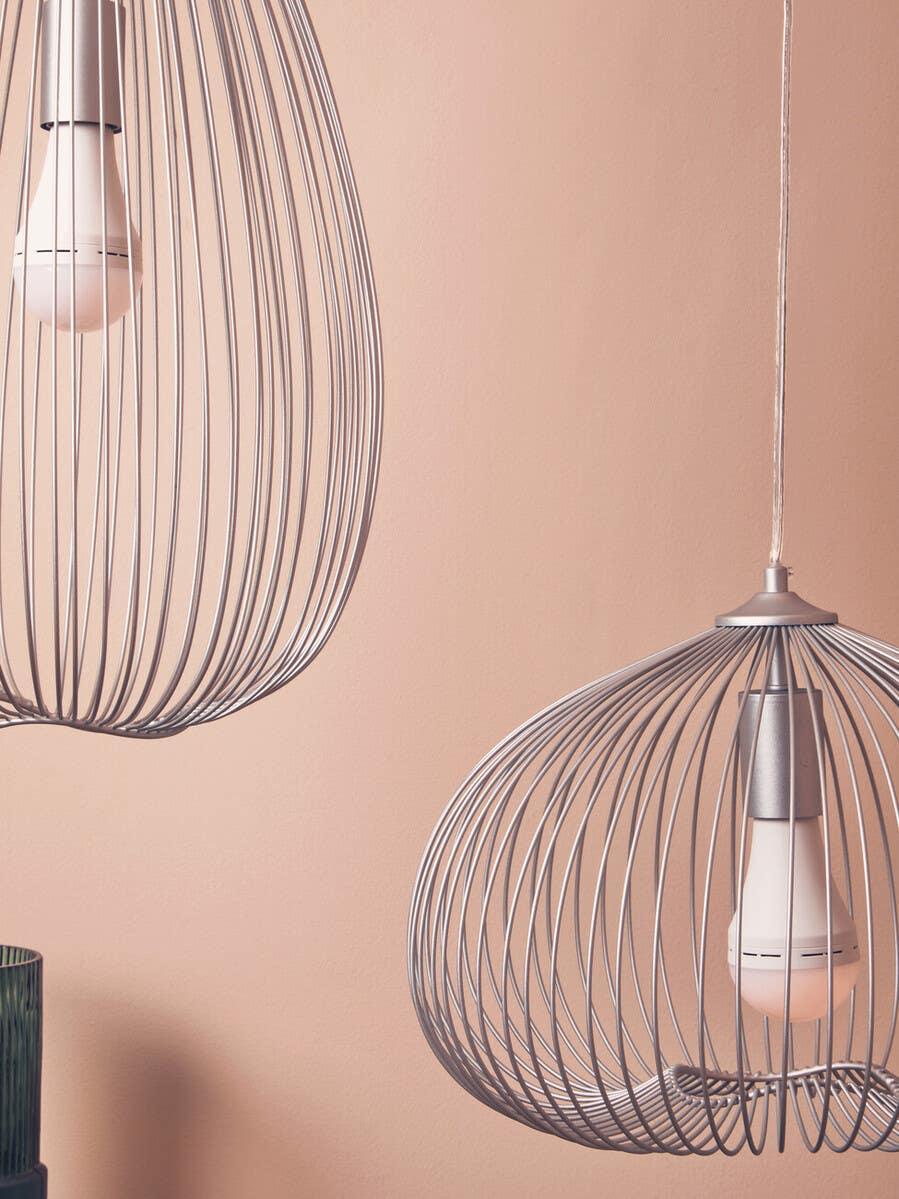 Pair of modern metal wire pendant lights with exposed bulbs against a peach wall