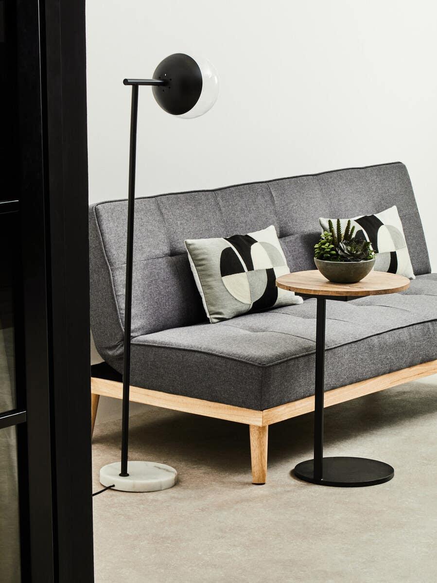 Grey fabric sofa with wooden legs, geometric cushions, round side table and modern floor lamp