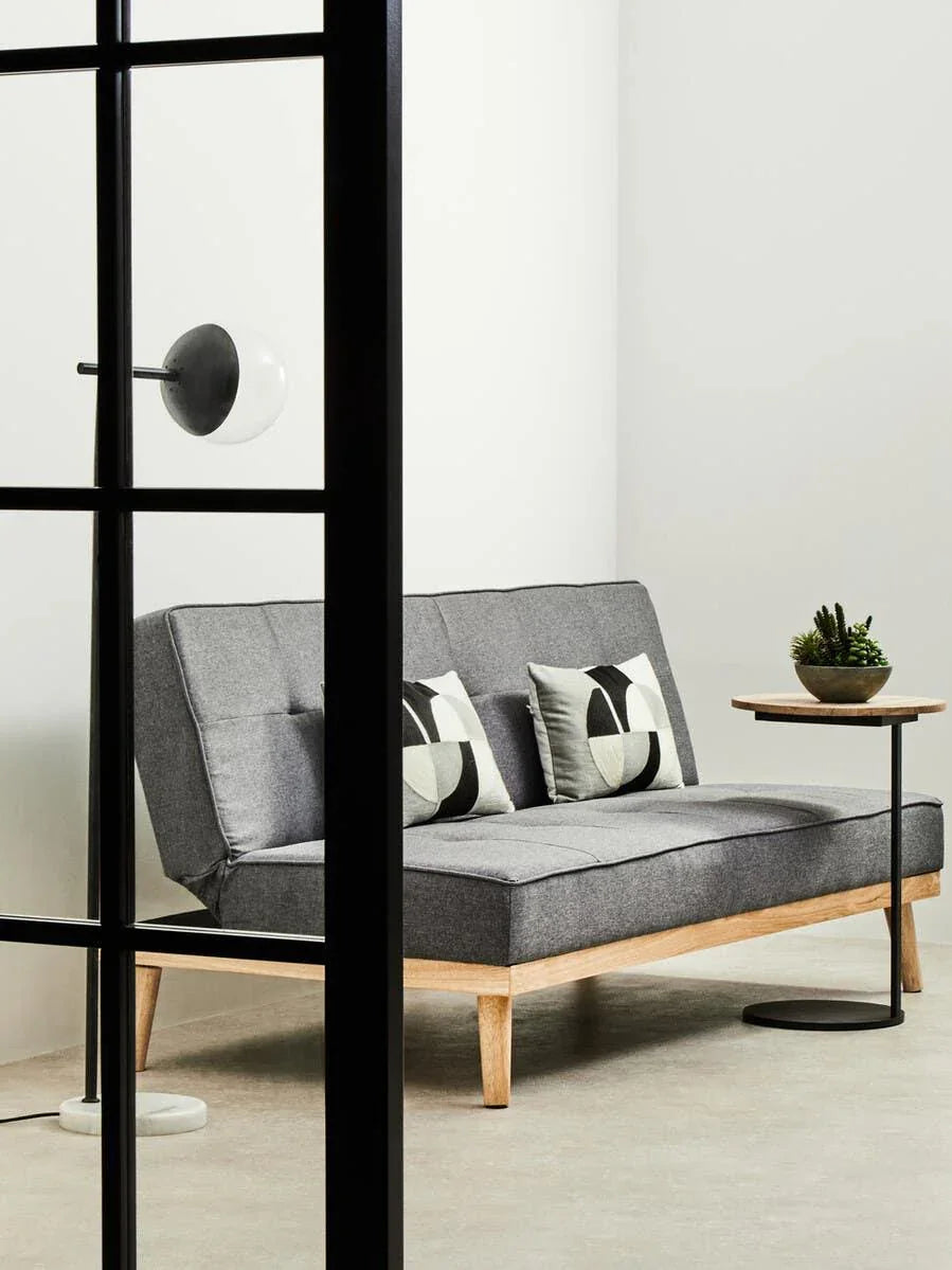 Grey fabric sofa with wooden legs, two geometric cushions, side table, and indoor plant