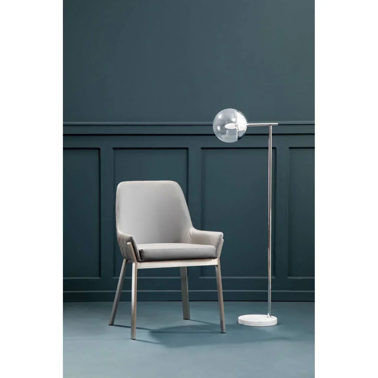 Modern grey accent chair with metal legs next to glass globe floor lamp against blue panelled wall