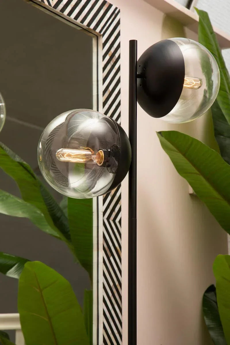 Modern floor lamp with black stem and clear glass globes beside large green indoor plants
