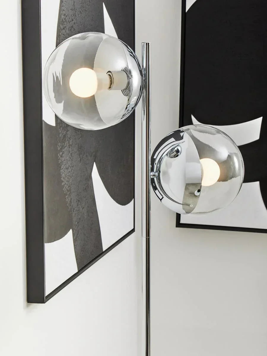 Chrome floor lamp with two glass globe shades beside abstract black and white wall art