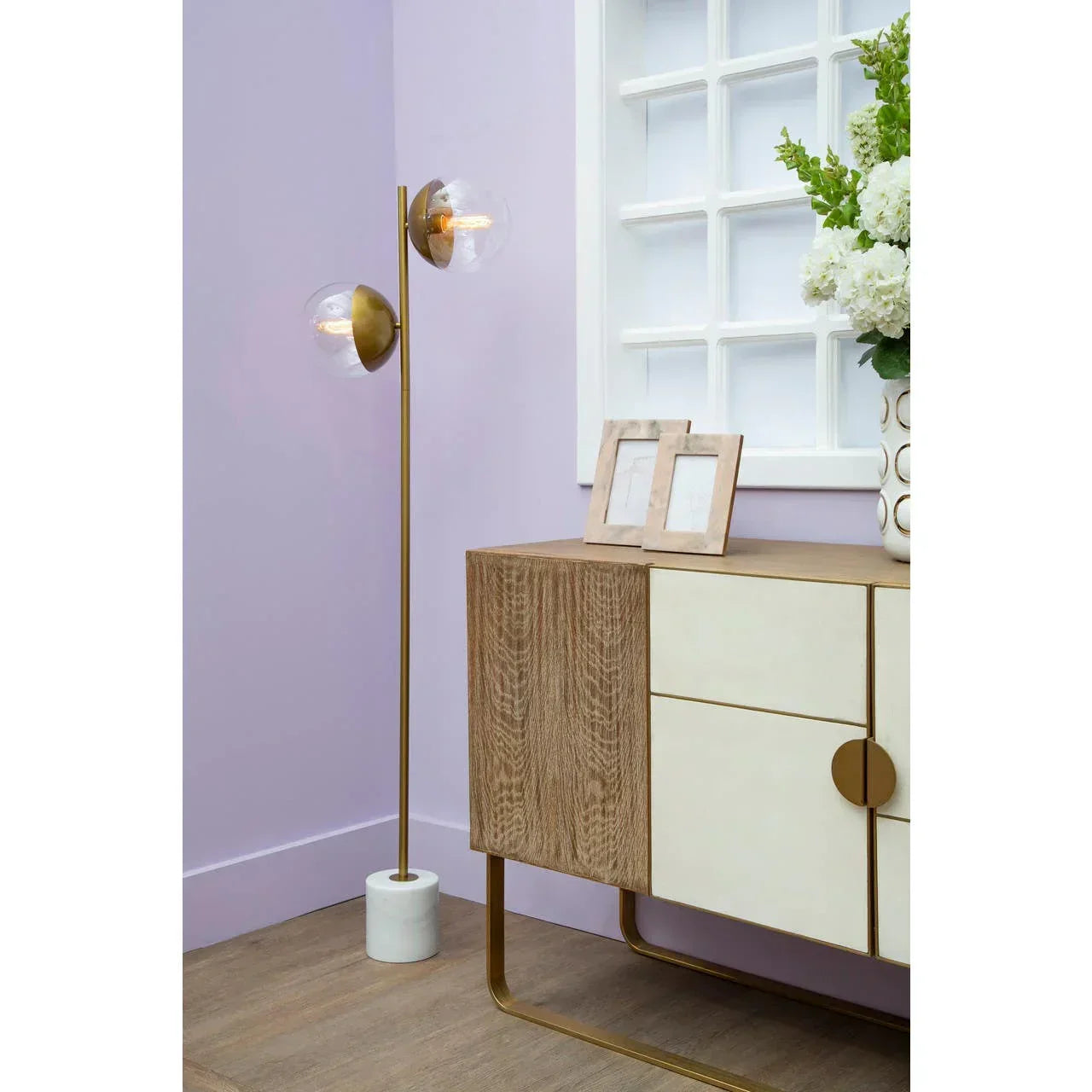 Modern wood and cream sideboard with brass handles beside gold floor lamp and flowers
