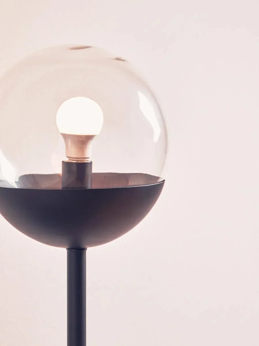 Modern floor lamp with round glass shade and black metal base against light wall