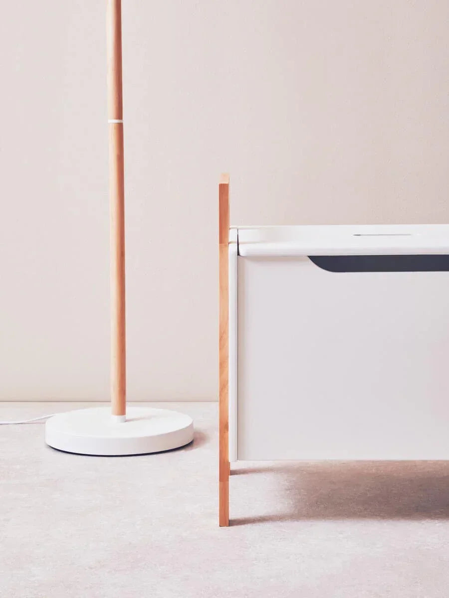 Modern white floor lamp beside minimalist wooden bed frame on light carpet