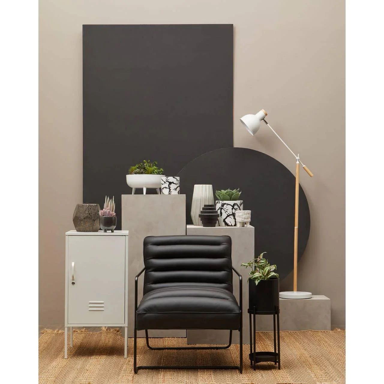 Black leather accent chair with metal frame beside indoor plants and white floor lamp