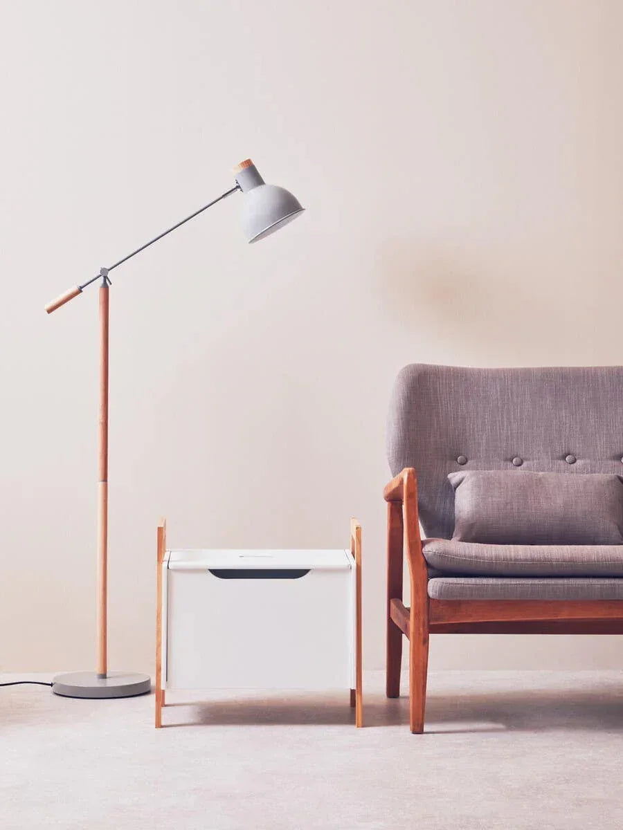 Modern grey armchair with cushion, wooden side table, and floor lamp in minimalist setting