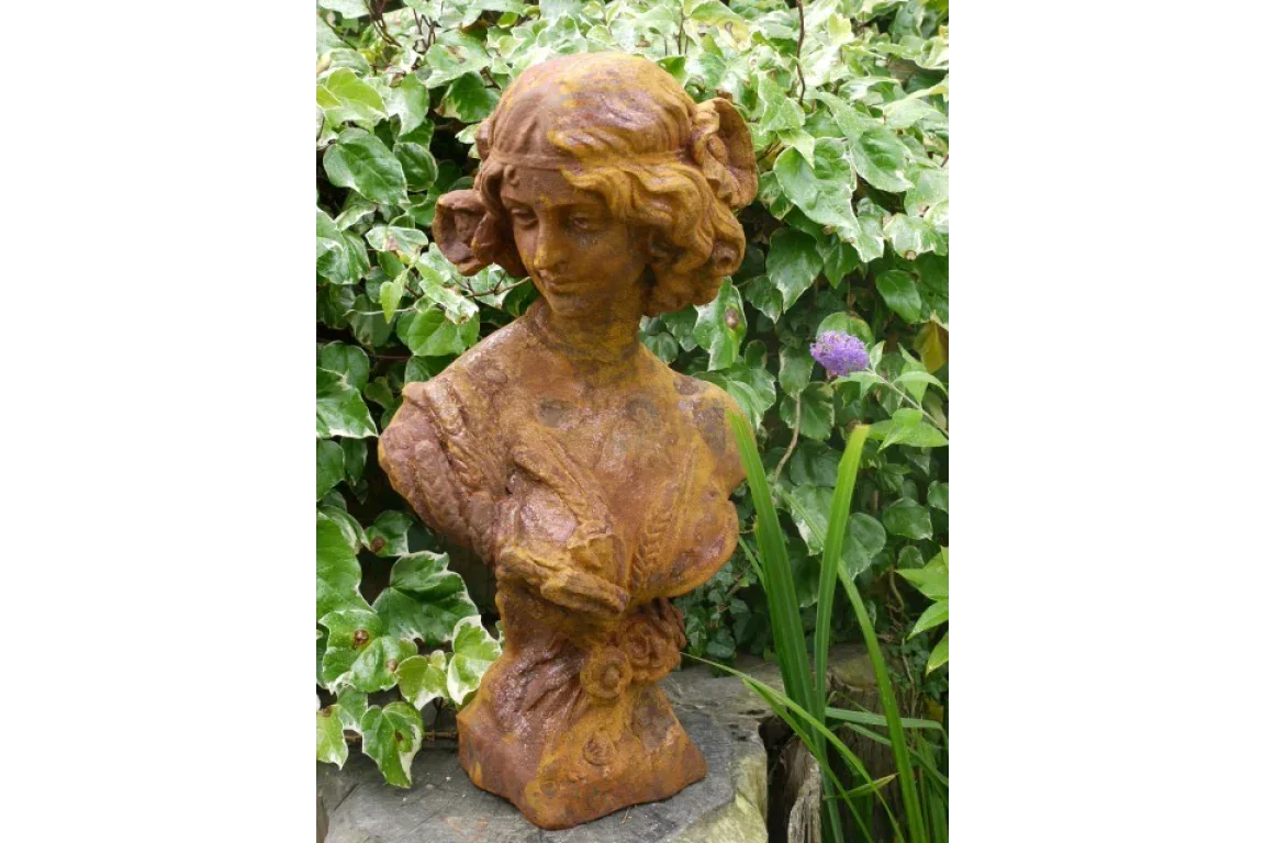 rust effect garden statue bust of woman on stone with leafy plants in background