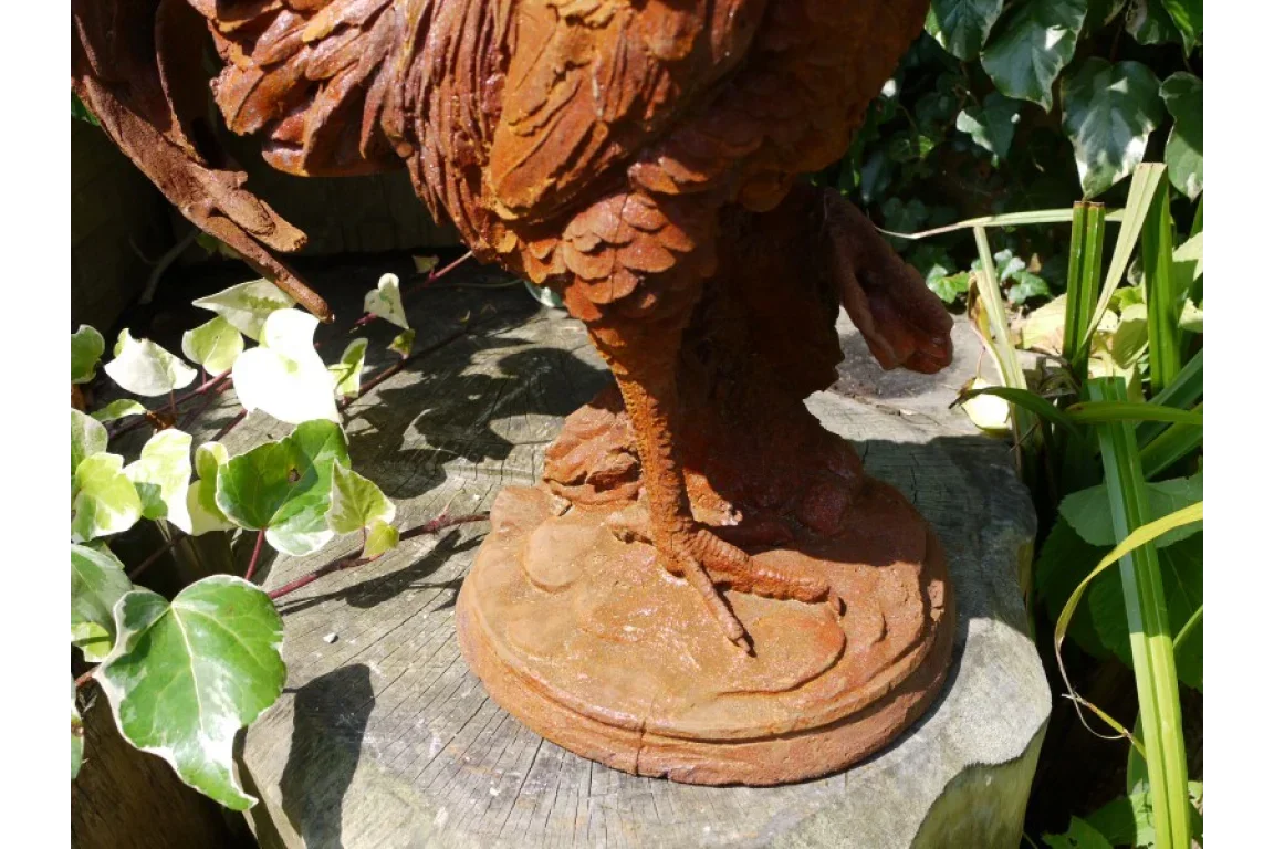 Rust effect metal garden ornament bird legs on weathered tree stump among green leaves