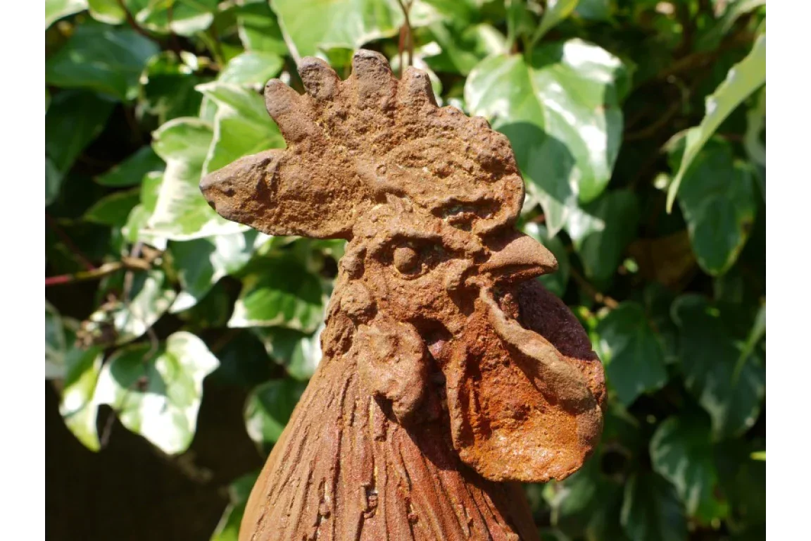 Rustic metal rooster garden ornament with textured finish and leafy background