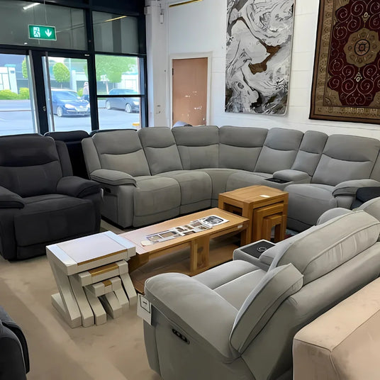 Grey fabric corner sofa set with recliners and wooden coffee tables in showroom