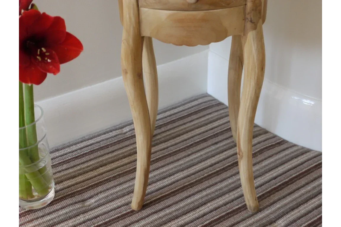 Natural wood side table legs with curved design on striped carpet beside glass vase with red flowers